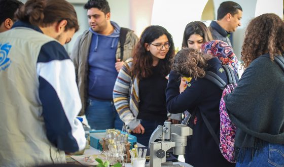 A collection of people talking behind a microscope at a trade fair